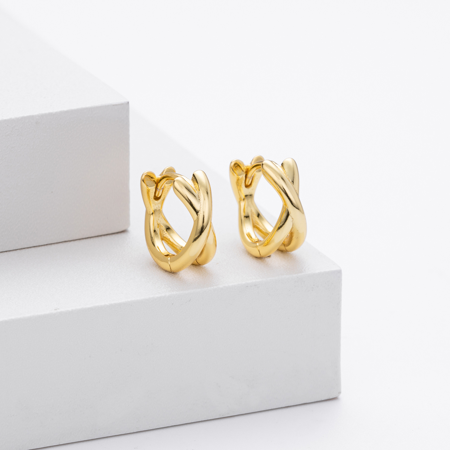 Close-up view of gold plated crisscross twisted huggie hoop earrings