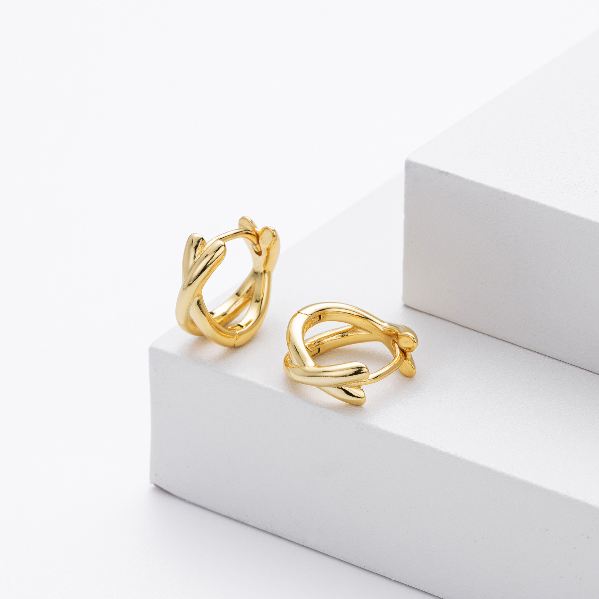 Side view of gold plated crisscross twisted huggie hoop earrings